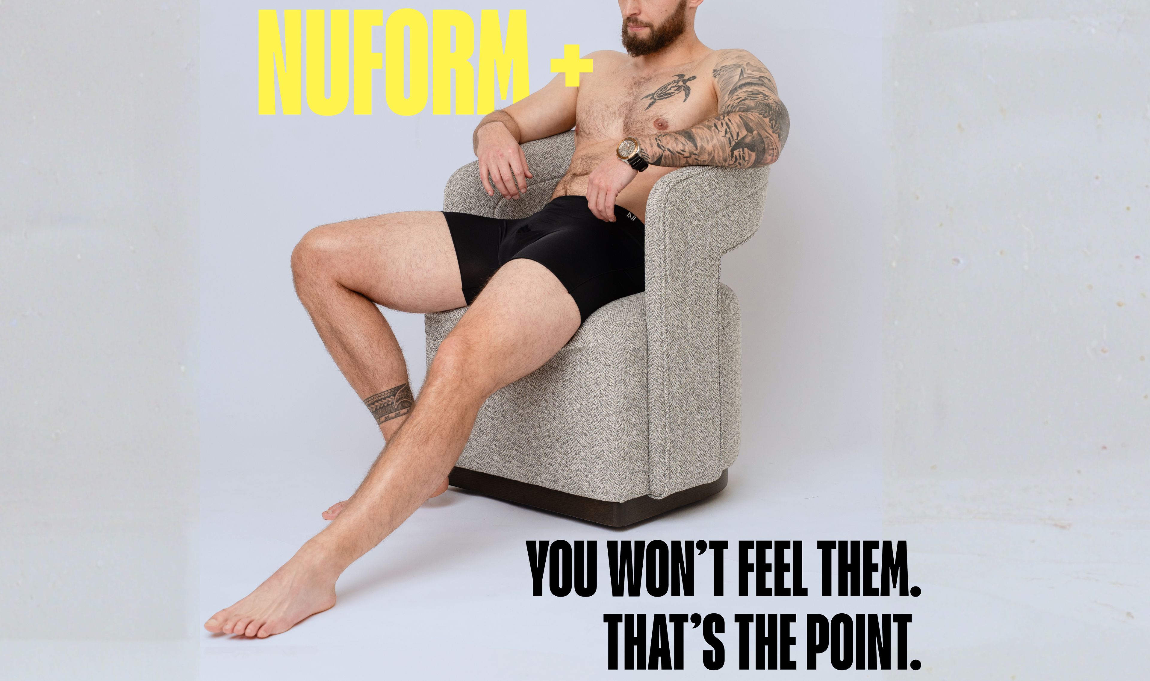 Man sitting on a chair wearing black underwear with 'NUFORM' branding and text.